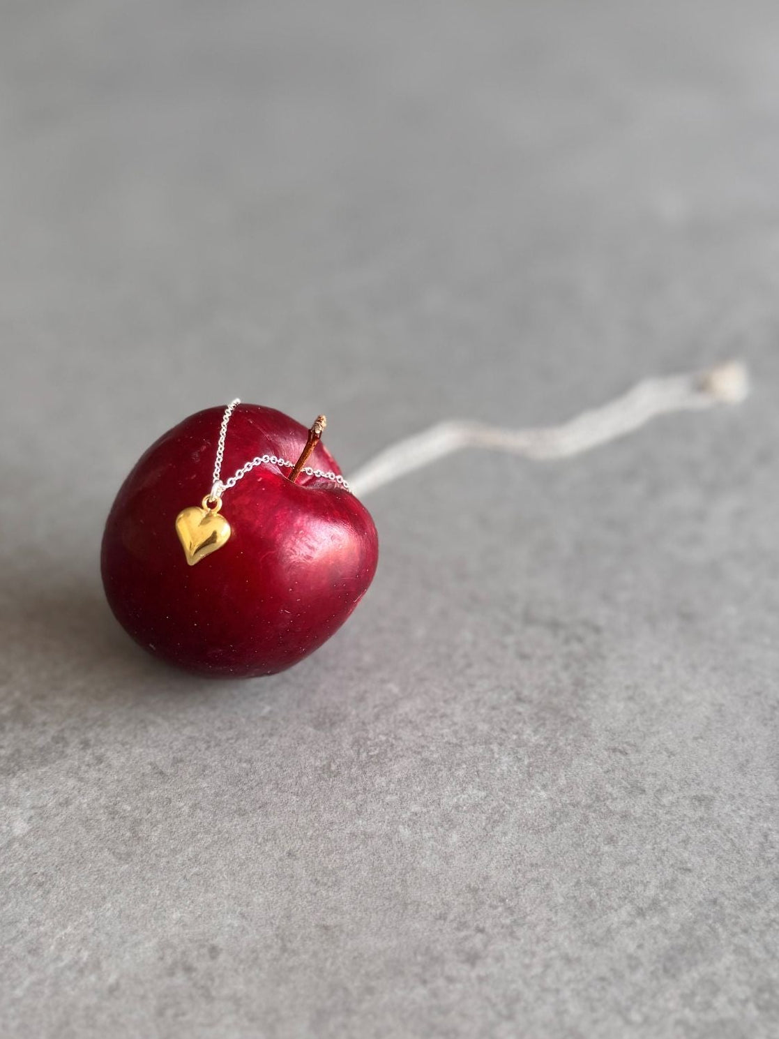 Red cherry with a gold heart charm necklace.