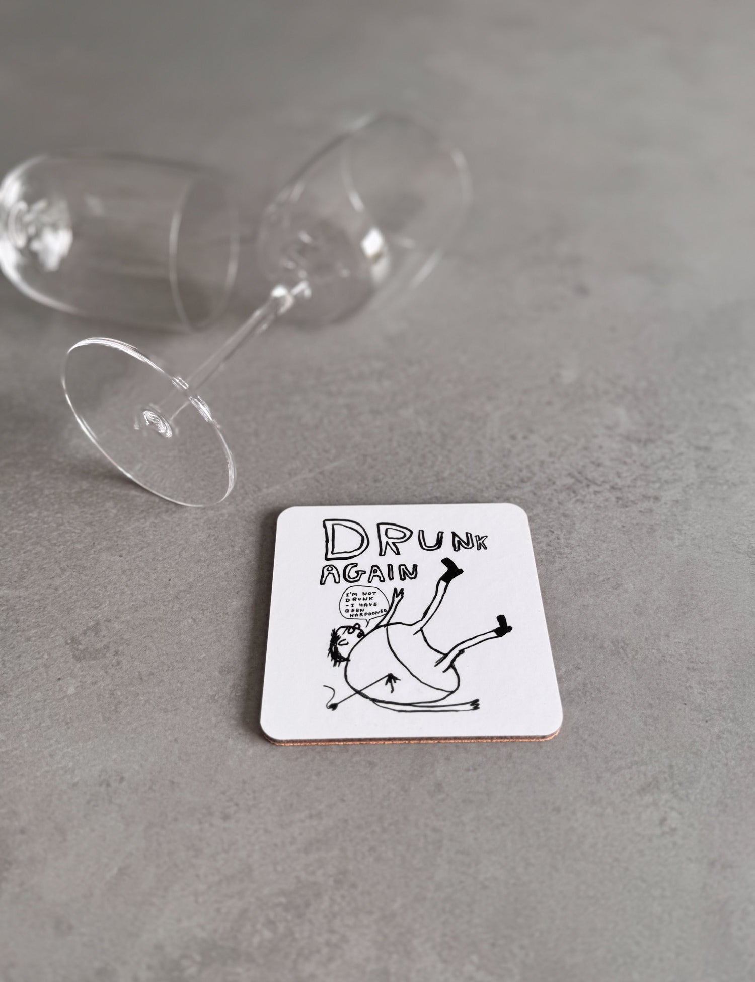Coaster with 'Drunk Again' text and illustration on a gray surface with a glass.
