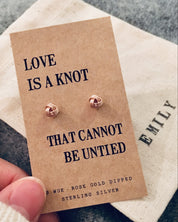 Rose gold earrings on a 'Love is a knot' card held by a hand.