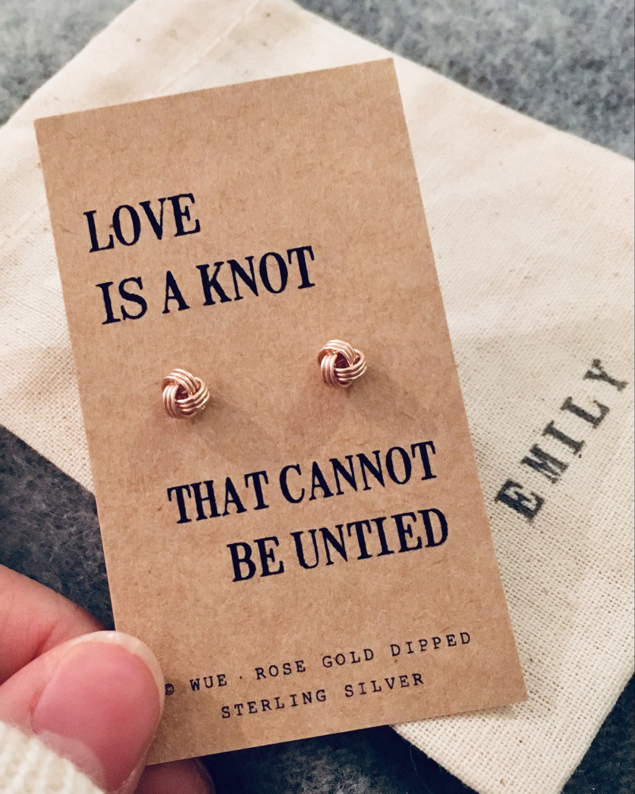 Rose gold earrings on a 'Love is a knot' card held by a hand.