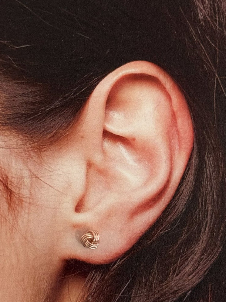 Close-up of an ear wearing a small rose gold knot earring 