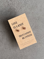 Pair of earrings on a card with 'Love is a knot that cannot be untied' text on a gray background